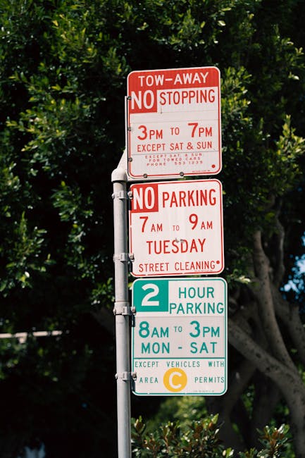 Two white outdoor signs placed among dense foliage and shrubs, with a dark background of leafy branches. The left sign displays a black silhouette of a dog crossed out with a red circle and line, alon
